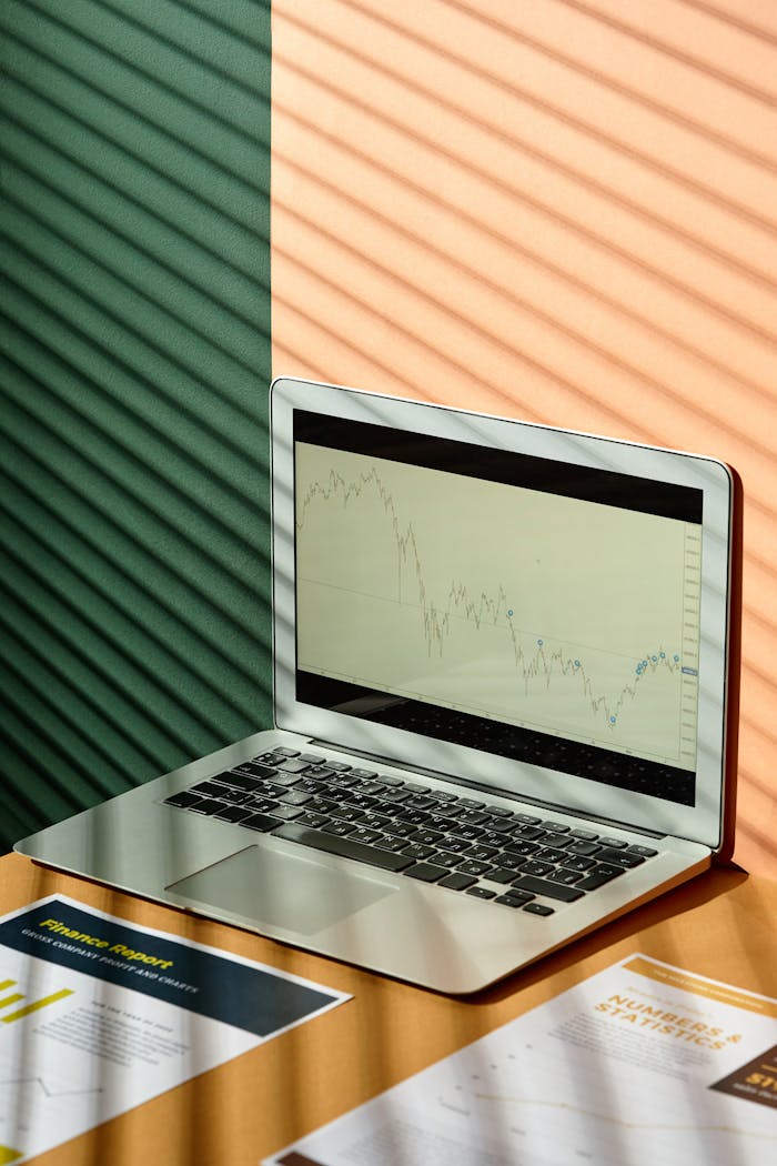 A laptop displaying financial graphs with documents on a sunlit office desk, ideal for finance themes.