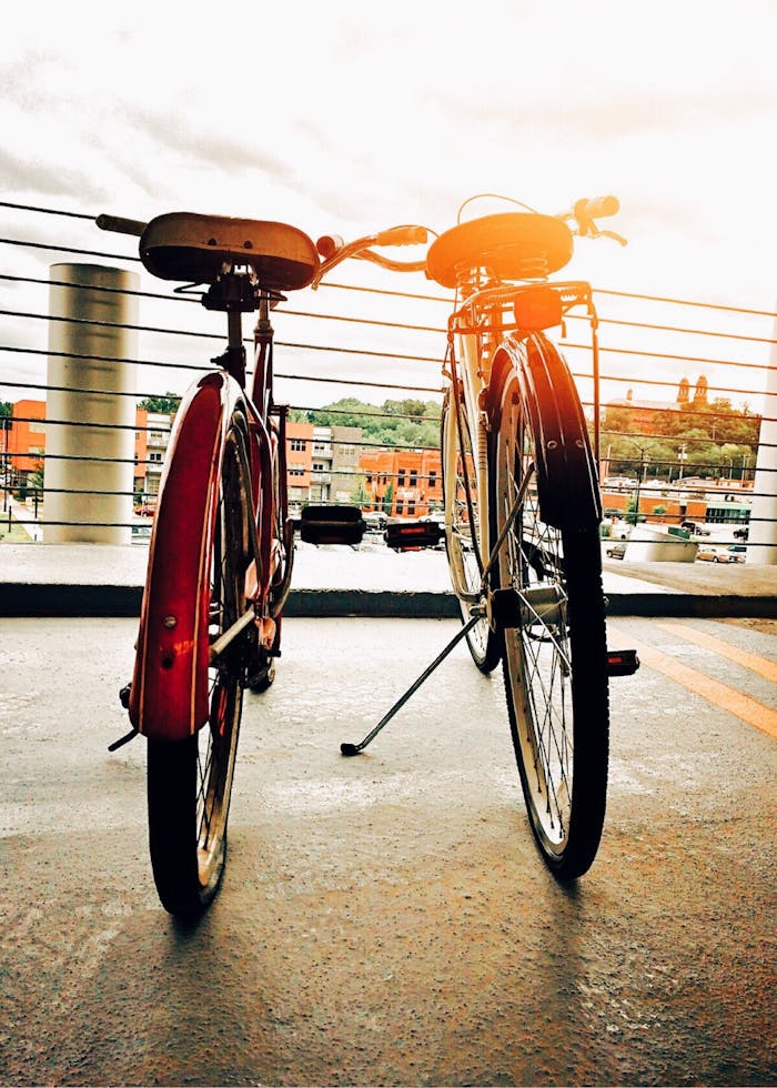 Two vintage bicycles parked on an urban rooftop during sunset, overlooking the cityscape.